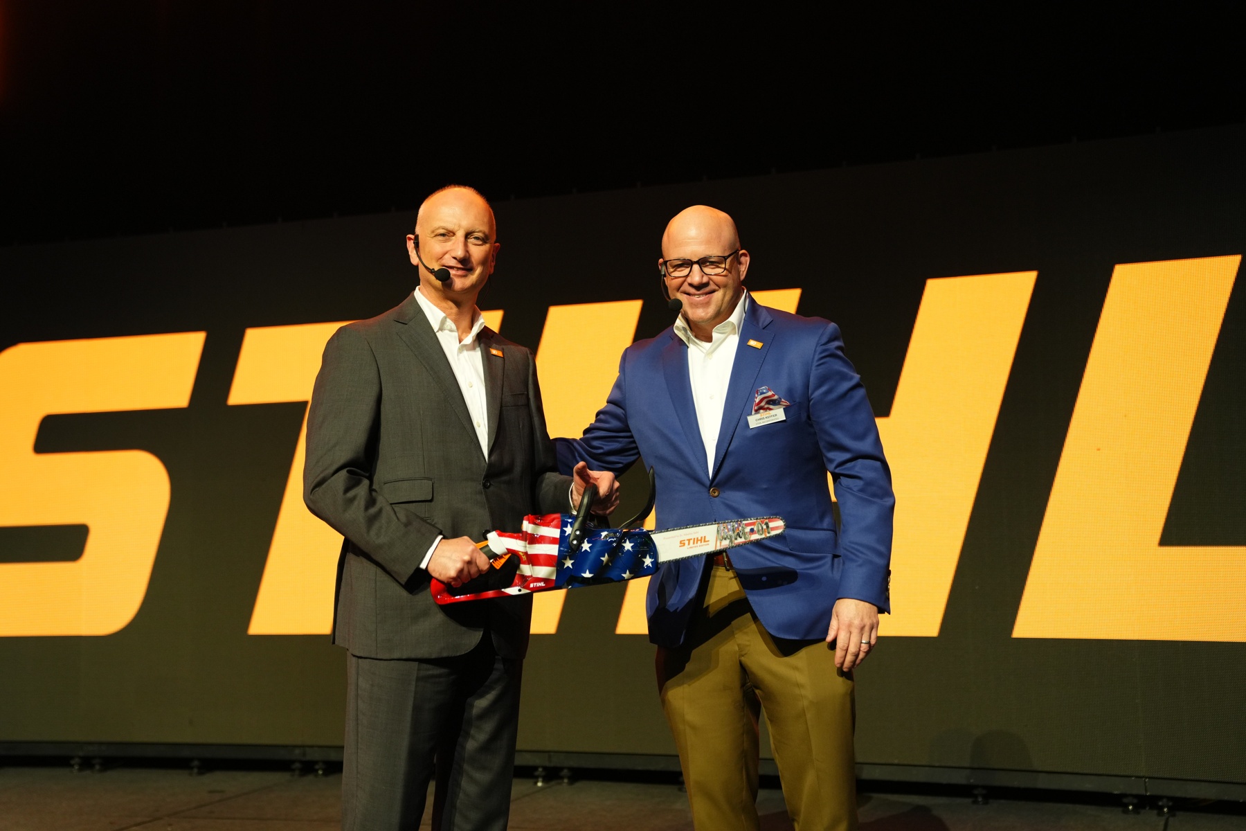 Dr. Nikolas Stihl (balra) és Chris Keffer, a STIHL Inc. amerikai ügyvezető igazgatója egy jubileumi fűrészt ajándékoz egy amerikai zászlóval.
